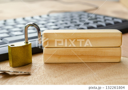 A bright brass padlock positioned on a desk near a computer keyboard with blank wooden blocks with customizable space for text. 132261804