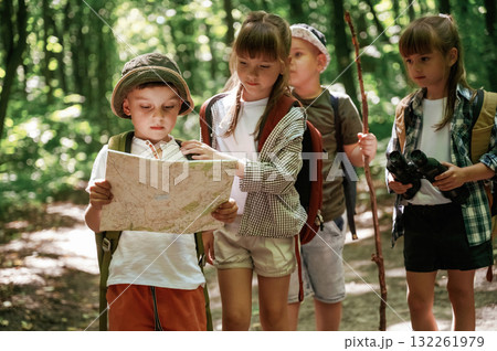 Smart boy is reading the map. Kids in forest at summer daytime together 132261979