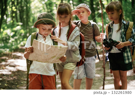 Smart boy is reading the map. Kids in forest at summer daytime together 132261980
