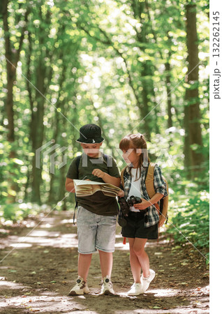 Checking the way on the map. Kids in forest at summer daytime together 132262145