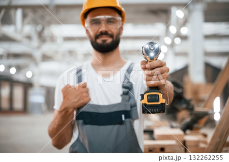With cordless impact driver. Industrial worker in wooden warehouse With cordless impact driver. Industrial worker in wooden warehouse 132262255