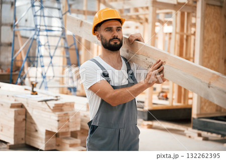 Front view, holding plank. Industrial worker in wooden warehouse 132262395