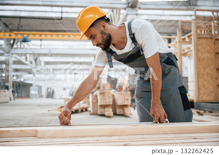 Standing, marking plank by pencil. Industrial worker in wooden warehouse Standing, marking plank by pencil. Industrial worker in wooden warehouse 132262425