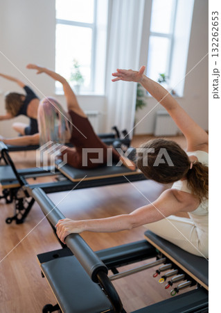 Pilates group of Women doing mermaid exercise in a sunlite modern studio, embodying calm, focus, and strength. 132262653