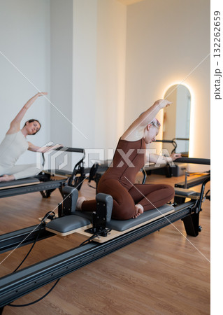 Pilates group of Women doing mermaid exercise in a sunlite modern studio, embodying calm, focus, and strength. Pilates group of Women doing mermaid exercise in a sunlite modern studio, embodying calm, focus, and strength. 132262659