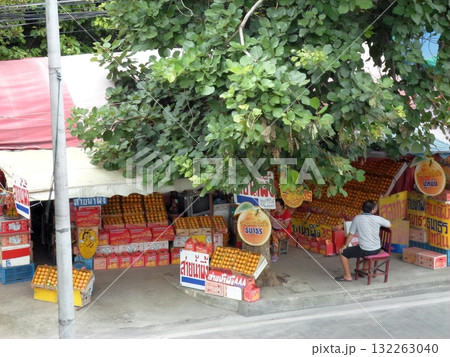 Outdoor Fruit Stall with Oranges and a Vendor Under a Shady Tree 132263040