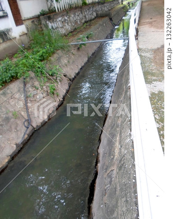 Narrow Irrigation Canal with Stone Walls and White Fencing in a Quiet Area Narrow Irrigation Canal with Stone Walls and White Fencing in a Quiet Area 132263042