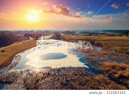 Aerial view of the countryside and frozen winding brook in the evening at sunset light. Beautiful natural landscape with cloudy sky 132263101