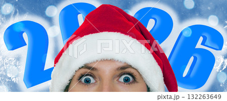 Young woman wearing a Santa hat on frozen blue background. 2026 inscription. Young woman wearing a Santa hat on frozen blue background. 2026 inscription. 132263649