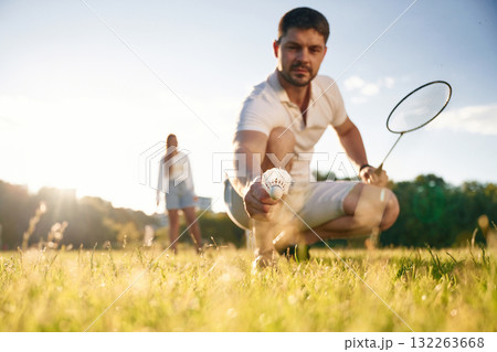Fallen shuttlecock, guy is taking it. Man with woman are playing badminton on the field 132263668