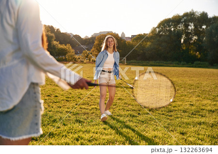 Two women are having fun, with badminton rackets, on the field Two women are having fun, with badminton rackets, on the field 132263694