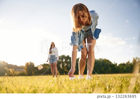 Picking up the fallen shuttlecock. Two women are having fun, with badminton rackets, on the field Picking up the fallen shuttlecock. Two women are having fun, with badminton rackets, on the field 132263695