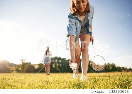 Picking up the fallen shuttlecock. Two women are having fun, with badminton rackets, on the field 132263698