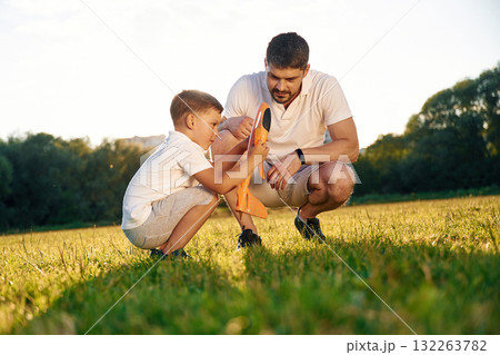 Fixing the broken toy plane. Father and little son are together on the summer field Fixing the broken toy plane. Father and little son are together on the summer field 132263782