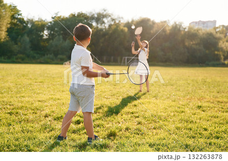 Rackets in hands, playing badminton. Happy kids are on the summer field Rackets in hands, playing badminton. Happy kids are on the summer field 132263878