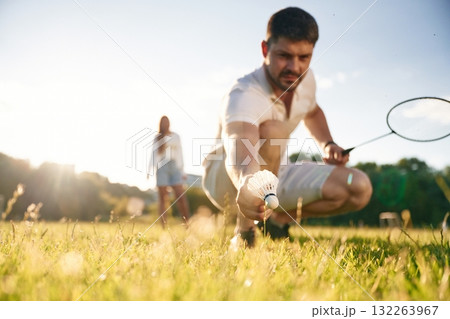 Guy is picking up the shuttlecock. Man with woman are playing badminton on the field 132263967