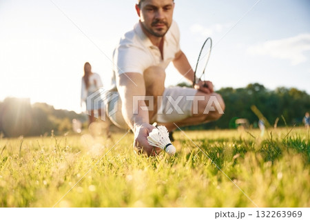 Fallen shuttlecock, guy is taking it. Man with woman are playing badminton on the field 132263969