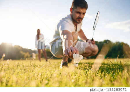 Fallen shuttlecock, guy is taking it. Man with woman are playing badminton on the field 132263971