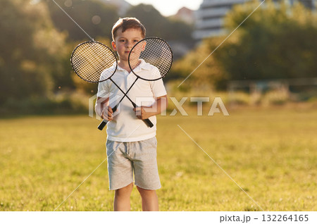 Happy little boy is with two tennis or badminton rackets on the summer field 132264165