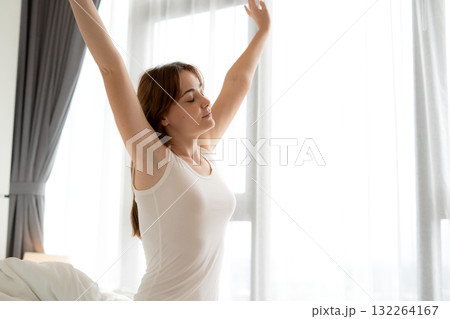 Happy young caucasian woman stretching hand on bed in morning, wellness lifestyle routine. Happy young caucasian woman stretching hand on bed in morning, wellness lifestyle routine. 132264167