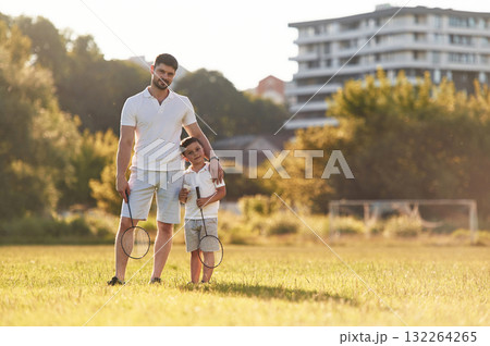 With badminton rackets. Father and little son are together on the summer field 132264265