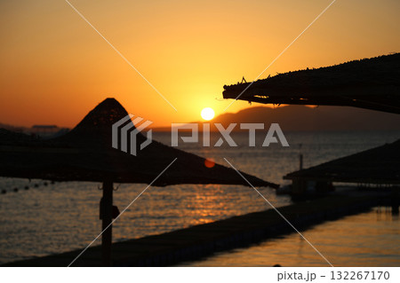 Sunrise over the sea against the backdrop of thatched umbrellas on the beach Sunrise over the sea against the backdrop of thatched umbrellas on the beach 132267170