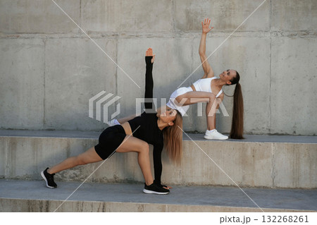 Front view, stretching exercises. Two sportive women are outdoors together Front view, stretching exercises. Two sportive women are outdoors together 132268261
