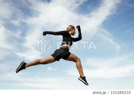 Jumping against the sky. Beautiful fitness woman in sport clothes is outdoors Jumping against the sky. Beautiful fitness woman in sport clothes is outdoors 132268310