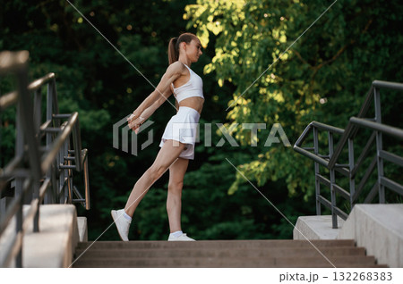 In white sport clothes. Young skinny fitness woman is outdoors 132268383