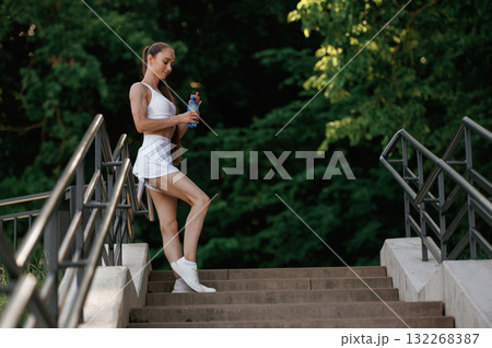 With bottle of water. Young skinny fitness woman is outdoors With bottle of water. Young skinny fitness woman is outdoors 132268387