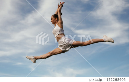 Blue sky with clouds, jumping. Young skinny fitness woman is outdoors 132268403