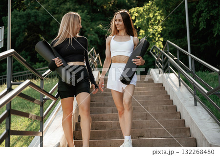 Carrying yoga mats. Two sportive women are outdoors together 132268480