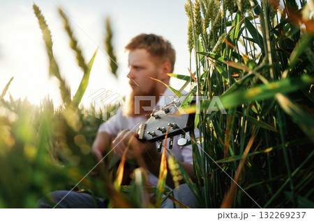 Country musician is with guitar on the ground. Man in white shirt is on the agricultural field Country musician is with guitar on the ground. Man in white shirt is on the agricultural field 132269237