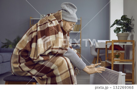 Senior man sitting in a cold room at home and warming up his hands by an electric heater 132269368