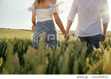 View from the back, holding hands, walking. Lovely couple are on the green agricultural field together View from the back, holding hands, walking. Lovely couple are on the green agricultural field together 132269412