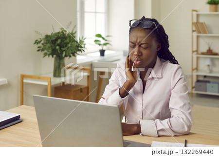 Woman sitting at the desk of her workplace in office or at home suffering from toothache. Woman sitting at the desk of her workplace in office or at home suffering from toothache. 132269440