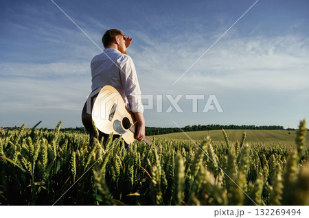 Musician is with acoustic guitar. Man in white shirt is on the agricultural field Musician is with acoustic guitar. Man in white shirt is on the agricultural field 132269494