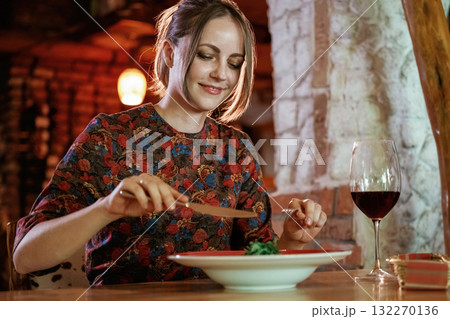 Uses a fork and a knife. Woman is in the restaurant with food and drink Uses a fork and a knife. Woman is in the restaurant with food and drink 132270136