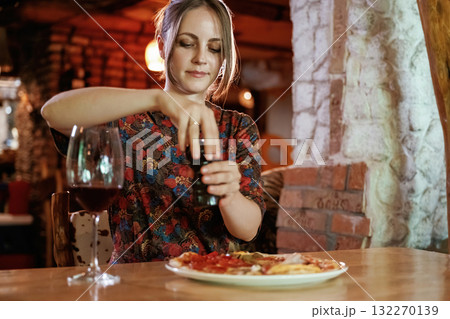 Adding pepper to the meal. Woman is in the restaurant with food and drink 132270139