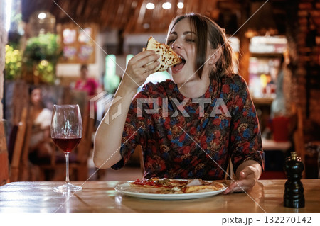 Delicious slice of pizza. Woman is in the restaurant with food and drink 132270142