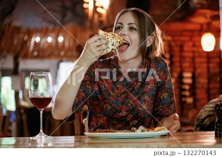 Delicious slice of pizza. Woman is in the restaurant with food and drink 132270143