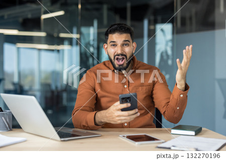 Businessman stares at his smartphone in shock and frustration, mouth agape and hand outstretched as he reacts to bad news at his office desk, stressed and overwhelmed Businessman stares at his smartphone in shock and frustration, mouth agape and hand outstretched as he reacts to bad news at his office desk, stressed and overwhelmed 132270196