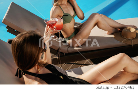 Wellness, holding red cocktails. Two beautiful women are resting near the pool Wellness, holding red cocktails. Two beautiful women are resting near the pool 132270463