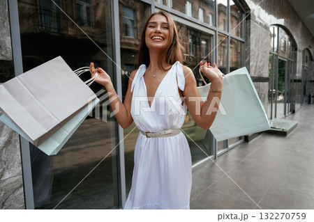 Showing the new stuff, smiling. Stylish woman is with shopping bag outdoors near the building Showing the new stuff, smiling. Stylish woman is with shopping bag outdoors near the building 132270759