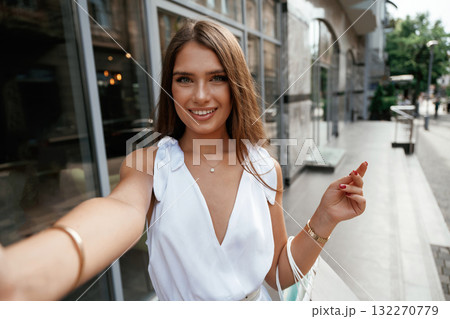 Making a selfie, smiling. Stylish woman is with shopping bag outdoors near the building Making a selfie, smiling. Stylish woman is with shopping bag outdoors near the building 132270779
