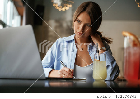 Writing information by a pen. Beautiful woman with laptop is in the bar Writing information by a pen. Beautiful woman with laptop is in the bar 132270843