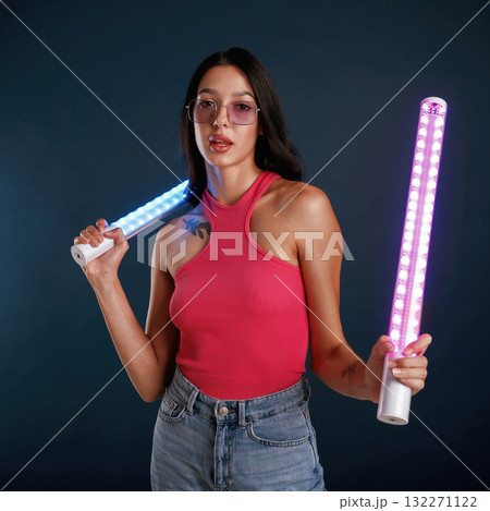 Neon lighting equipment in hands. Beautiful young woman is against background Neon lighting equipment in hands. Beautiful young woman is against background 132271122