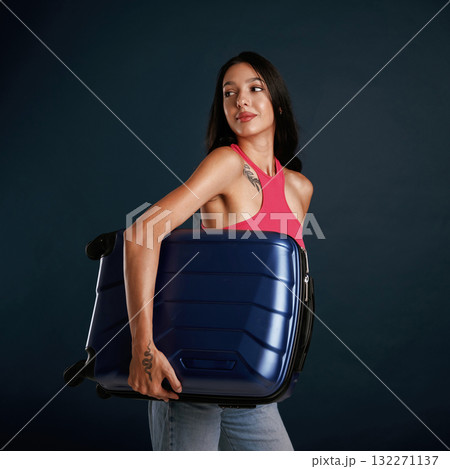Holds a suitcase. Beautiful young woman is against background 132271137