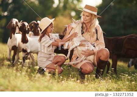 On the ground. Mother and daughter are together on the farm with goats On the ground. Mother and daughter are together on the farm with goats 132271352
