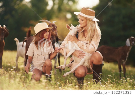 On the ground. Mother and daughter are together on the farm with goats 132271353